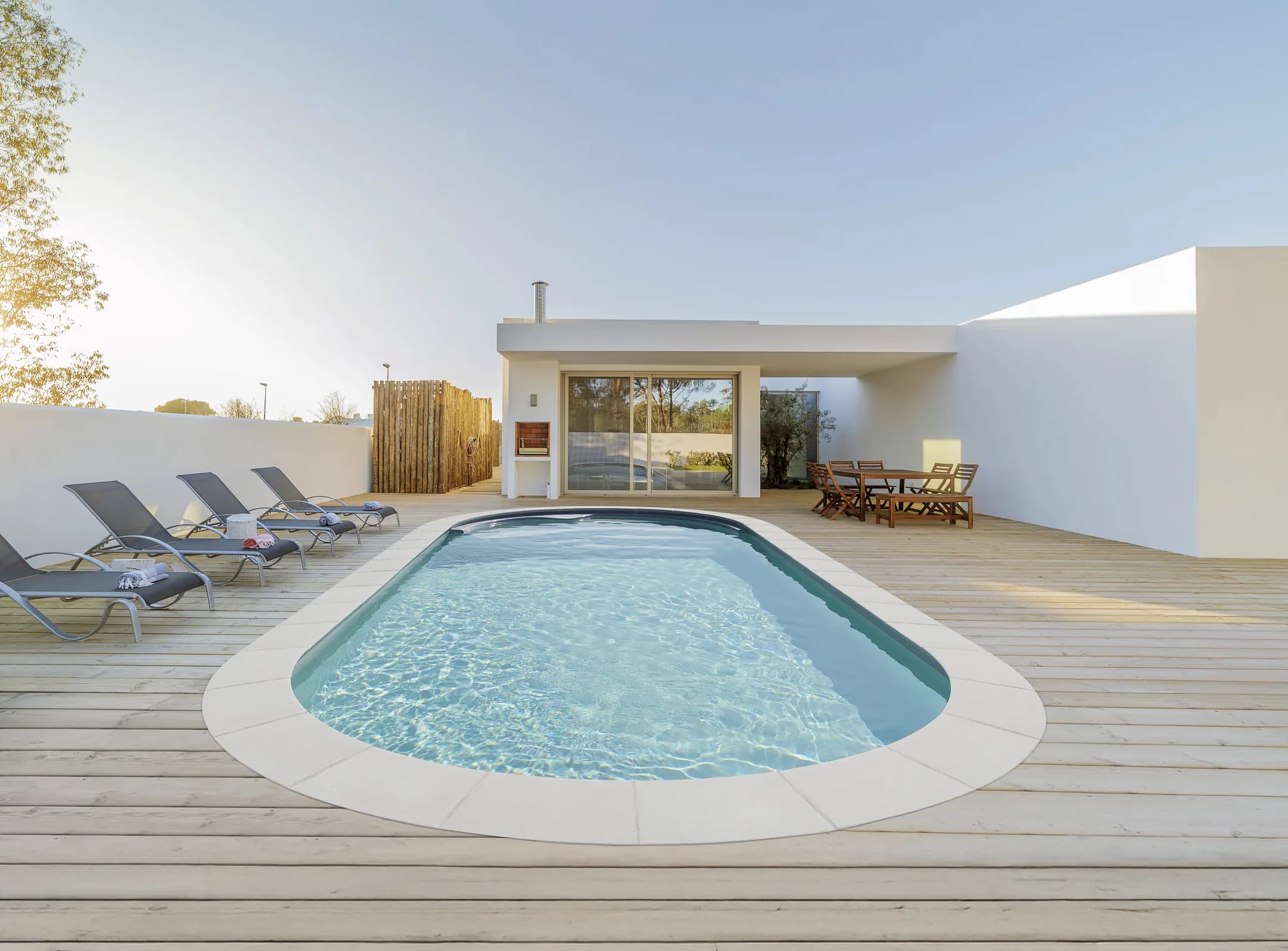 Geradliniger Pool mit heller Holzterrasse vor einem modernen Haus