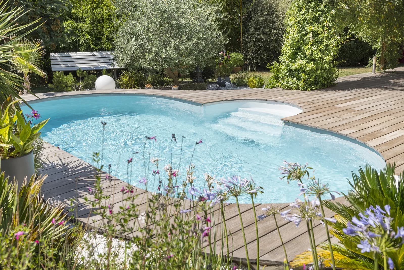 Ovaler Ilona-Pool mit Treppe und Holzterrasse in einem bepflanzten Garten