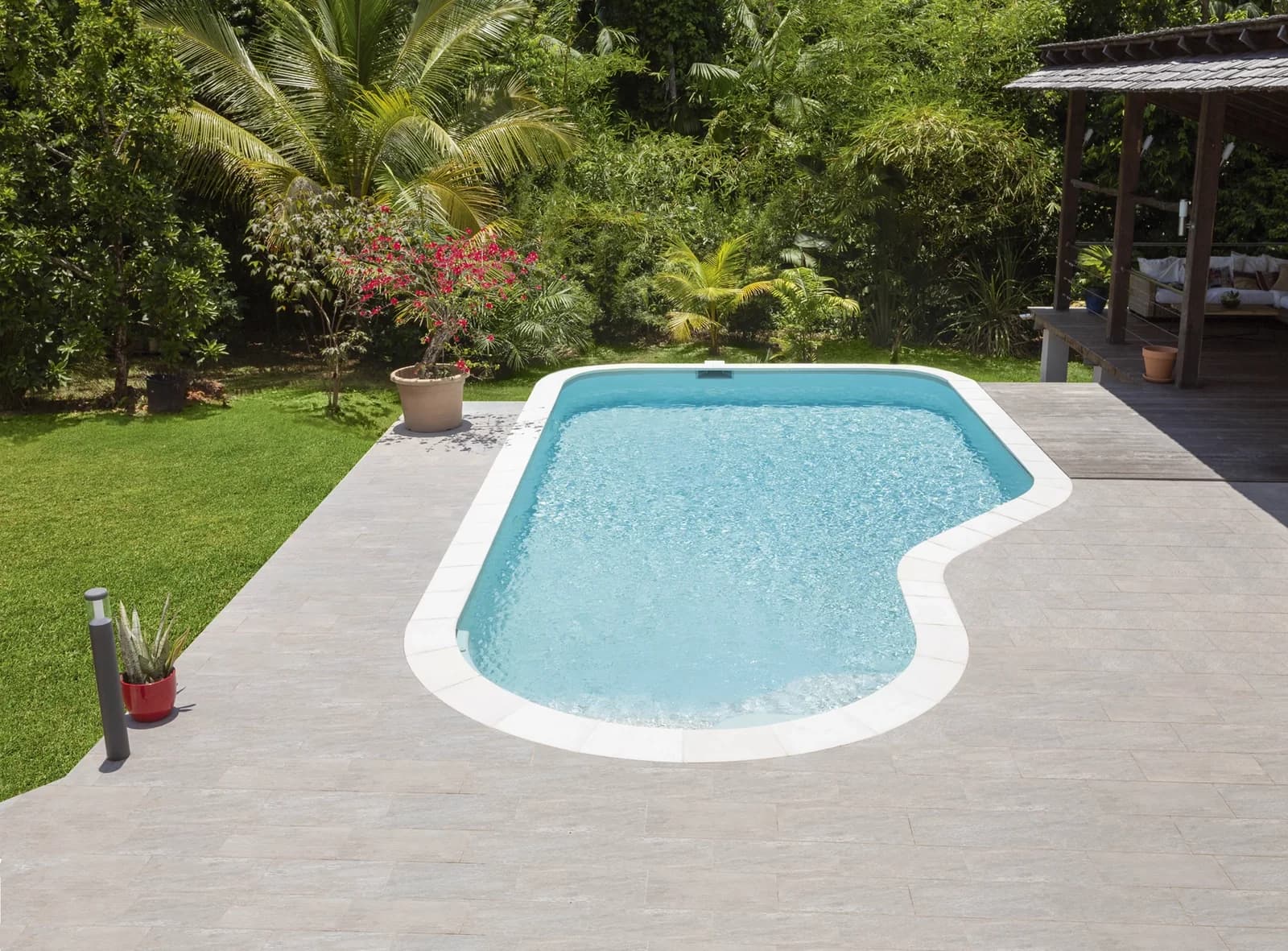 Geschwungener Maria-Pool mit heller Terrasse in einem Garten