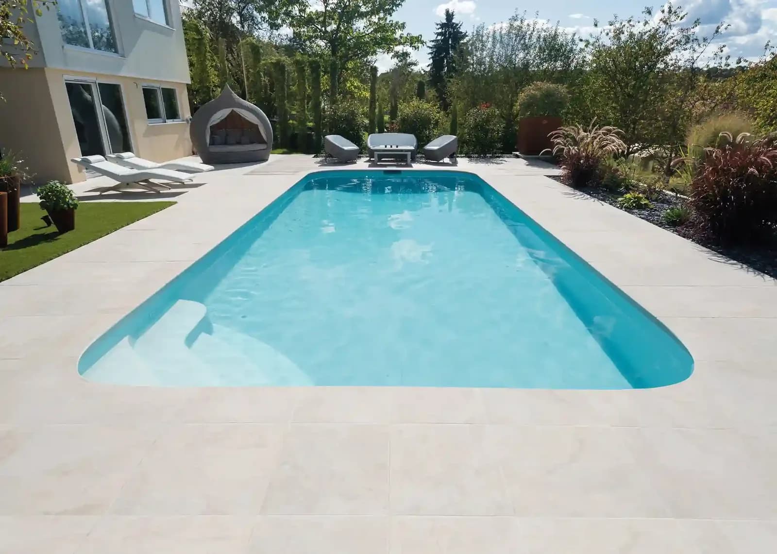 Romy-Pool mit heller Terrasse vor einem Wohnhaus